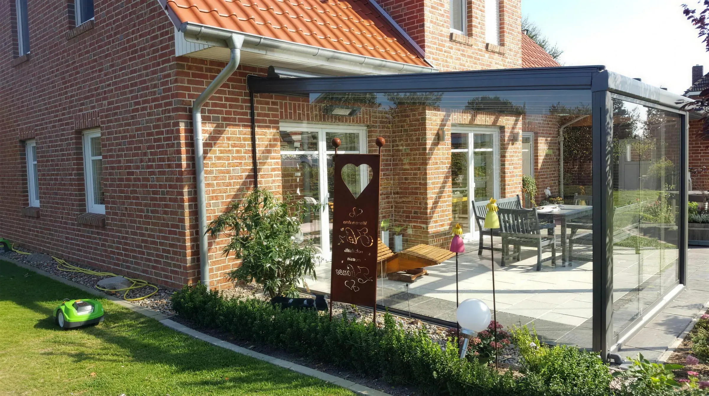 Terrassendach mit Glas-Schiebewänden an einem Klinkerhaus im Sonnenschein, gebaut von der Glaserei Laugesen in Verden