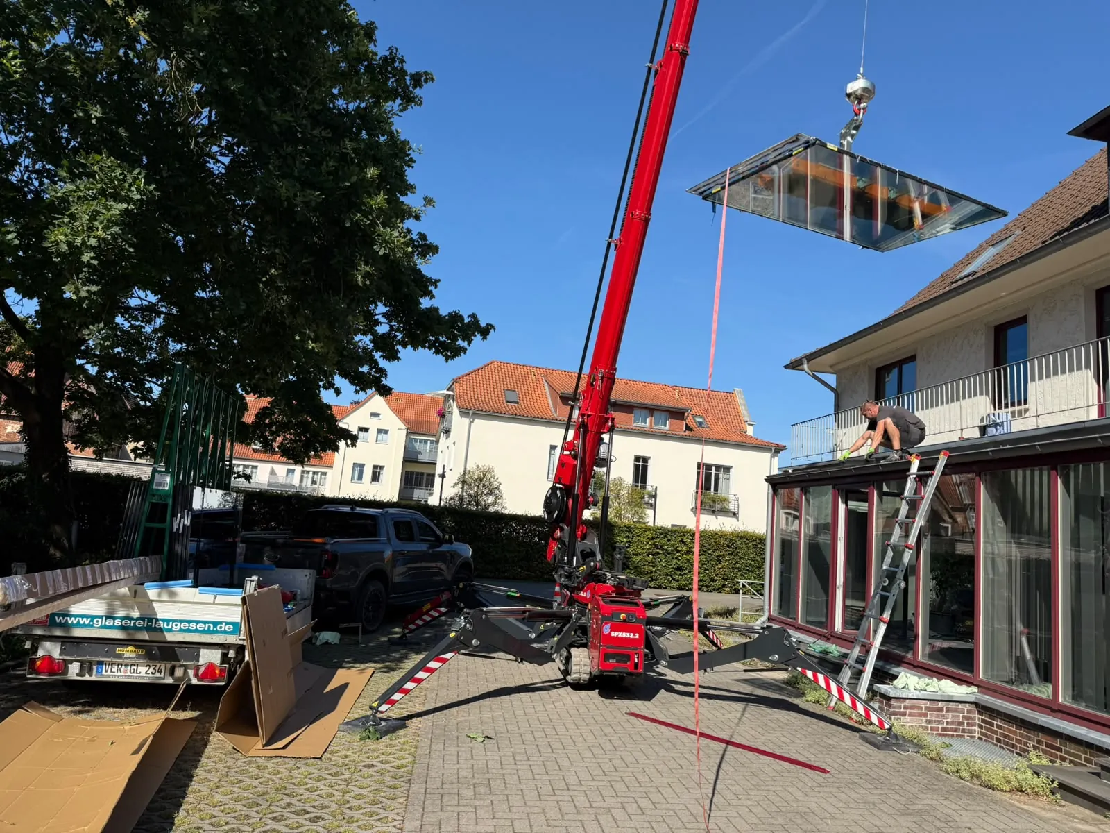 Mini-Kran der Glaserei Laugesen hebt ein großformatiges Glaselement über ein Wohnhaus in Verden